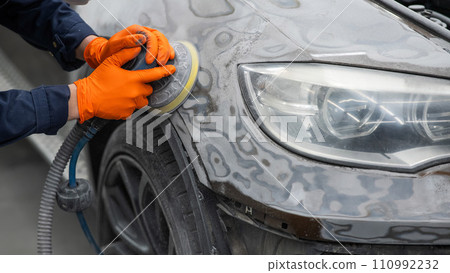 A mechanic sands the putty on a car body with a machine. Repair after an accident. A mechanic sands the putty on a car body with a machine. Repair after an accident. 110992232