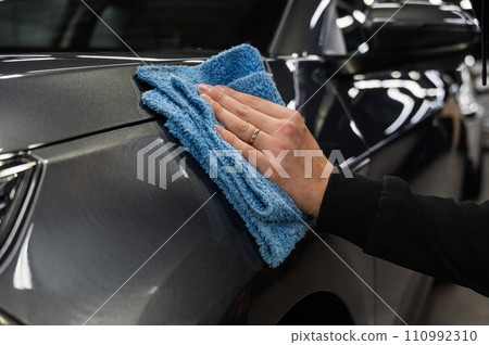 A man wipes the surface of the body of a gray car with a microfiber cloth. A man wipes the surface of the body of a gray car with a microfiber cloth. 110992310