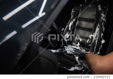 Man cleaning black leather car seat with brush and cleaning foam.  110992315