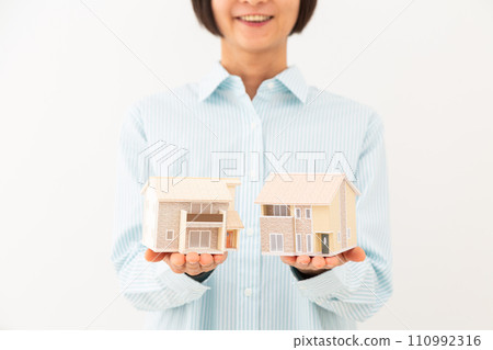 A middle-aged woman smiling while holding a house model 110992316