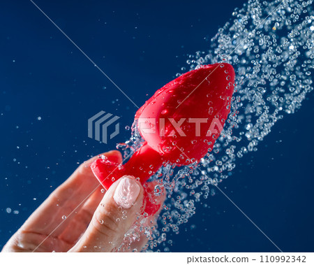 Woman washing red anal plug under shower on blue background. Woman washing red anal plug under shower on blue background. 110992342