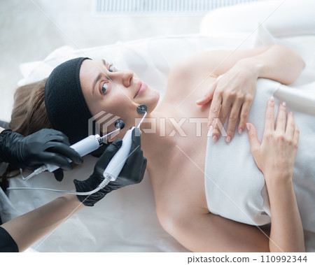 Young caucasian woman on microcurrent therapy procedure. Beautician's office. Young caucasian woman on microcurrent therapy procedure. Beautician's office. 110992344