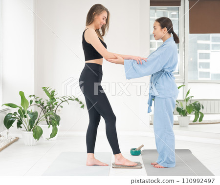 Caucasian woman stands on sadhu boards with therapist support. 110992497