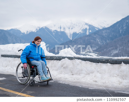 Caucasian woman in a wheelchair travels in the mountains in winter. 110992507