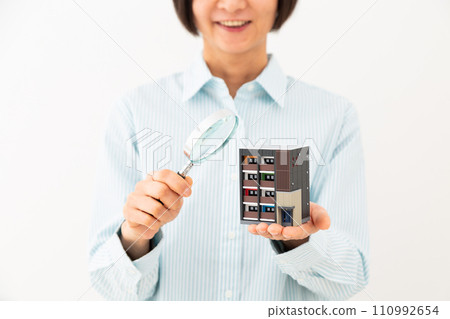 A middle-aged woman smiling while holding a model of an apartment and a magnifying glass A middle-aged woman smiling while holding a model of an apartment and a magnifying glass 110992654
