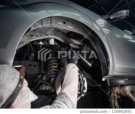 An auto mechanic applies anti-corrosion mastic to the underbody of a car. 110992691