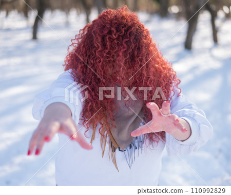 The plump-cheeked woman threw her red hair over her face and held out her arms like a zombie. Girl fooling around in the park in winter. The plump-cheeked woman threw her red hair over her face and held out her arms like a zombie. Girl fooling around in the park in winter. 110992829