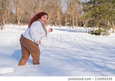 A fat red-haired woman in a white sweatshirt walks through snowdrifts.  110992836