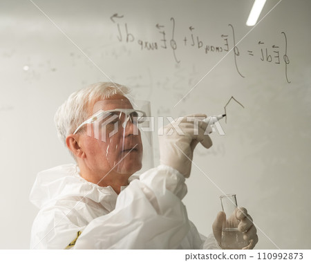 An elderly Caucasian male chemist in a protective suit writes on glass. An elderly Caucasian male chemist in a protective suit writes on glass. 110992873
