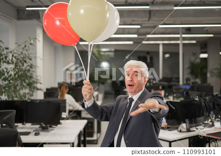 Portrait of a cheerful mature business man holding balloons in the office. Portrait of a cheerful mature business man holding balloons in the office. 110993101