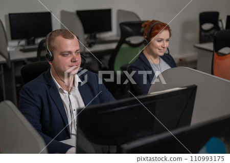 Two friendly call center employees talking to customers. Man and woman working with headsets in office. Two friendly call center employees talking to customers. Man and woman working with headsets in office. 110993175