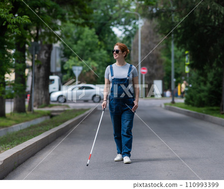 Blind pregnant woman walking down the street with a cane.  110993399