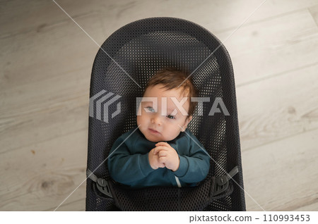 Cute newborn baby dressed in blue overalls sitting in a baby lounger. Cute newborn baby dressed in blue overalls sitting in a baby lounger. 110993453