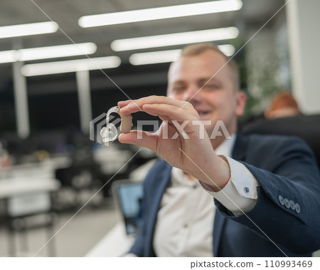 Deaf man working holds hearing aid while sitting in office. Deaf man working holds hearing aid while sitting in office. 110993469