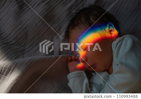 Close-up portrait of a newborn boy with a prism beam on his face. Rainbow. Close-up portrait of a newborn boy with a prism beam on his face. Rainbow. 110993488
