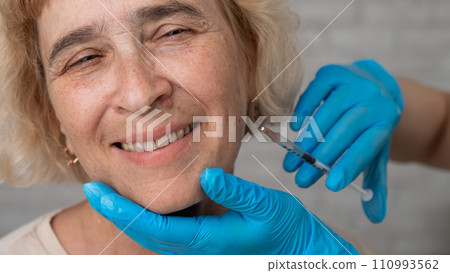 Doctor makes beauty injections in the face of an old caucasian woman. Doctor makes beauty injections in the face of an old caucasian woman. 110993562