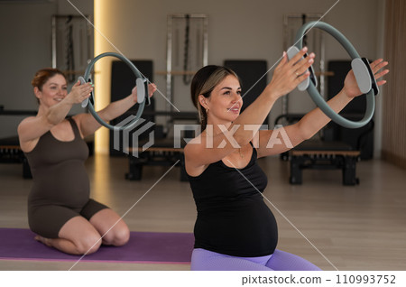 Two pregnant women doing yoga. Exercises with a gymnastic circle for Pilates.  110993752