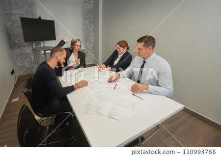 Four business people sitting around a table discussing blueprints. Designers engineers at a meeting. Four business people sitting around a table discussing blueprints. Designers engineers at a meeting. 110993768