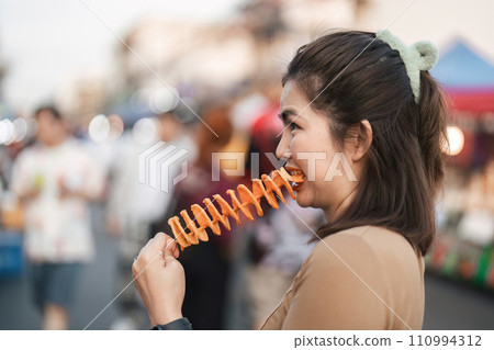 Happy young Asian Traveler foodie woman enjoy eating Tornado potatoes fries at outdoor night market street food Happy young Asian Traveler foodie woman enjoy eating Tornado potatoes fries at outdoor night market street food 110994312
