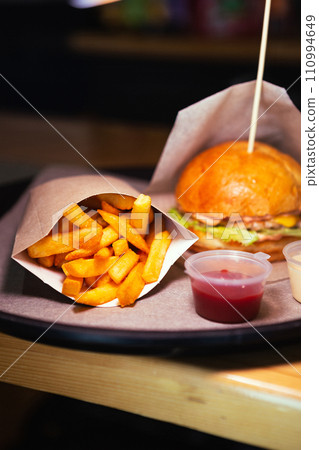 Side view of fresh cheeseburger with chicken and fries with red sauce on wooden table. High quality photo. Selective focus. Unhealthy eating concept 110994649