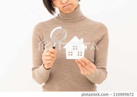 一位中年婦女拿著房屋模型和放大鏡,憂心忡忡。 一位中年婦女拿著房屋模型和放大鏡,憂心忡忡。 110995672