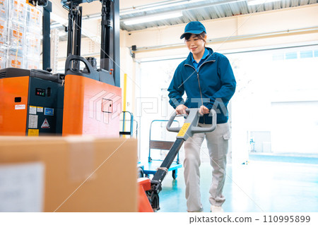A female worker using a hand lift in a warehouse A female worker using a hand lift in a warehouse 110995899