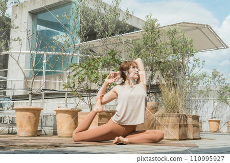 A woman doing yoga, Pilates, and stretching on the rooftop (pigeon pose) A woman doing yoga, Pilates, and stretching on the rooftop (pigeon pose) 110995927