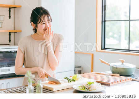 一位年輕女子、妻子、家庭主婦，一邊煮飯一邊在廚房說話 110995939