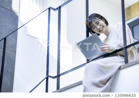 A woman sitting on an indoor bridge and using a laptop A woman sitting on an indoor bridge and using a laptop 110996610