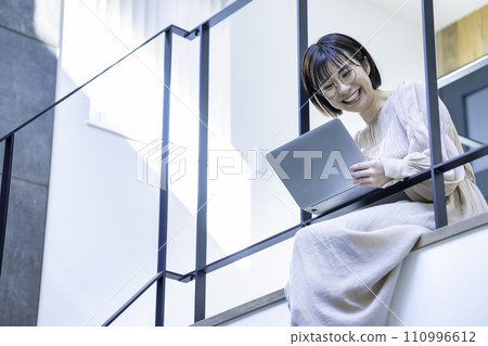 A woman sitting on an indoor bridge and using a laptop A woman sitting on an indoor bridge and using a laptop 110996612