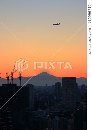 View of Mt. Fuji as seen from central Tokyo at sunset with a plane flying above in the orange sky View of Mt. Fuji as seen from central Tokyo at sunset with a plane flying above in the orange sky 110996713
