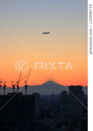 View of Mt. Fuji as seen from central Tokyo at sunset with a plane flying above in the orange sky View of Mt. Fuji as seen from central Tokyo at sunset with a plane flying above in the orange sky 110996714