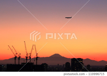 View of Mt. Fuji as seen from central Tokyo at sunset with a plane flying above in the orange sky View of Mt. Fuji as seen from central Tokyo at sunset with a plane flying above in the orange sky 110996715