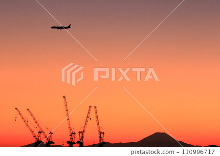 View of Mt. Fuji as seen from central Tokyo at sunset with a plane flying above in the orange sky 110996717