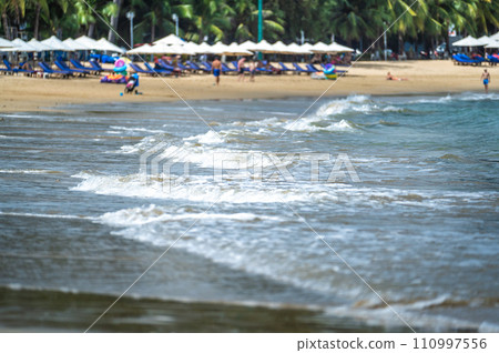 blurred backdrop of sandy beach unveils serene scene with gently lapping waves, sunbeds, and leisurely vacationers. coastal bliss captures essence of relaxation, forming tranquil haven by sea 110997556