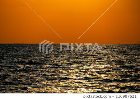 Fiery horizon, dramatic ocean sunset in vibrant hues over dark waters, nature breathtaking photo reflecting artistry of dusk's tranquil spectacle and coastal beauty 110997621