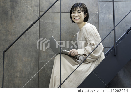 一位戴眼鏡的女士在樓梯上使用筆記型電腦 111002914