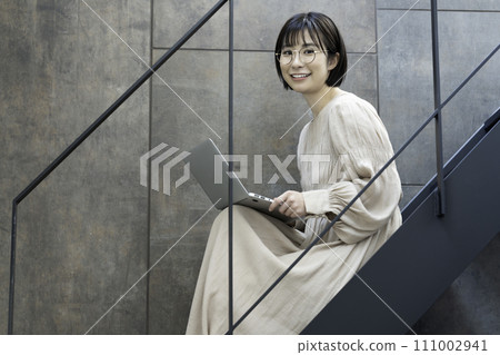 A woman wearing glasses using a laptop on the stairs A woman wearing glasses using a laptop on the stairs 111002941