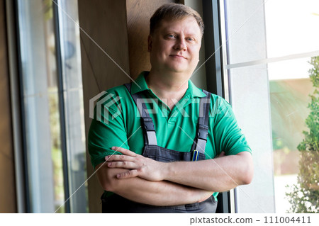 Portrait of a tired worker in overalls sitting by the window 111004411