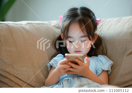 AI-generated content. Asian child sitting on a sofa, browsing internet on mobile device and playing with smartphone apps 111005112
