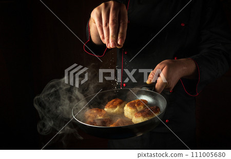 The cook adds salt to oladki in a frying pan. The concept of preparing a delicious Ukrainian national dish or bliny in the kitchen. Black space for advertising 111005680
