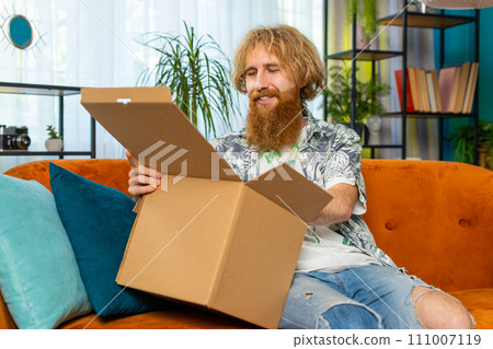 Happy redhead man shopper unpacking cardboard box delivery parcel online shopping purchase at home 111007119