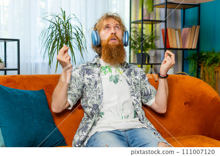 Redhead man listening music, breathes deeply meditating with concentrated thoughts peaceful at home 111007120