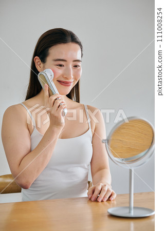 A woman in her 30s with long hair doing skin care using a facial beauty device A woman in her 30s with long hair doing skin care using a facial beauty device 111008254
