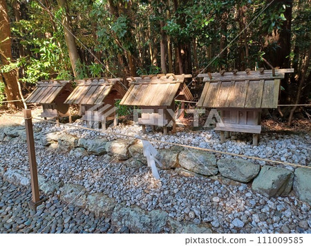 A deep forest lies behind four small shrines lined up in a sacred area separated by paper curtains. A deep forest lies behind four small shrines lined up in a sacred area separated by paper curtains. 111009585