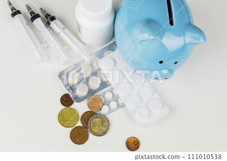 The blue piggy bank is surrounded by various medicines and euro coins The blue piggy bank is surrounded by various medicines and euro coins 111010538