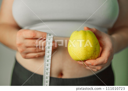 Person's hand holding green apple with grey measurement tape isolated on white background. Weight loss and dieting concept. Person's hand holding green apple with grey measurement tape isolated on white background. Weight loss and dieting concept. 111010723