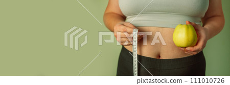 Person's hand holding green apple with grey measurement tape isolated on white background. Weight loss and dieting concept. Person's hand holding green apple with grey measurement tape isolated on white background. Weight loss and dieting concept. 111010726