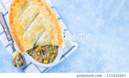Beef pot pie or deep dish pie in baking dish, crust broken open, horizontal, top view, copy space 111010841