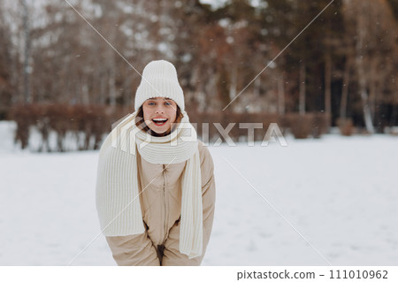Happy smiling young woman portrait dressed coat scarf hat and mittens enjoys winter weather at snowy winter park 111010962